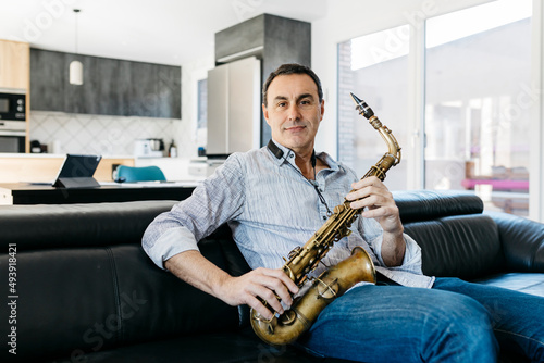 Smiling musician with saxophone sitting on sofa in living room at home photo