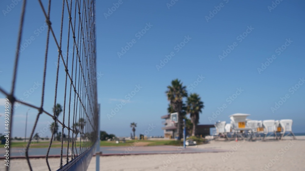 Volley ball net on court for volleyball game on beach, California coast, USA. Sport field or playground for players on sandy ocean shore, lifeguard station and palm trees on Mission beach, San Diego. Volley ball net on court for volleyball game on beach, California coast, USA. Sport field or playground for players on sandy ocean shore, lifeguard station and palm trees on Mission beach, San Diego.
