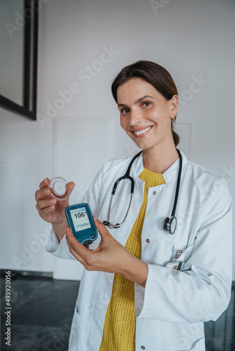 Smiling doctor holding blood glucose meter in clinic photo