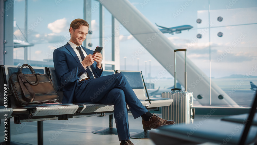 © Gorodenkoff - Airport Terminal Flight Wait: Smiling Businessman Uses Smartphone for e-Business, Browsing Internet with an App. Traveling Entrepreneur Work Online on Mobile Phone in Boarding Lounge of Airline Hub