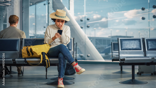 Airport Terminal: Black Woman Waits for Flight, Uses Smartphone, Receives Shockingly Bad News, Misses Flight. Upset, Sad, and Dissappointed Person Sitting in a Boarding Lounge of Airline Hub. photo