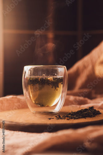 A glass cup of fragrant green tea on a wooden board next to scattered dry tea. steam over a hot drink. Brew tea.