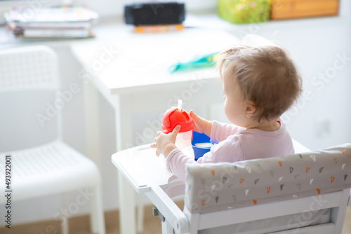 white baby girl takes a bottle of water at home kitchen background, water drinking