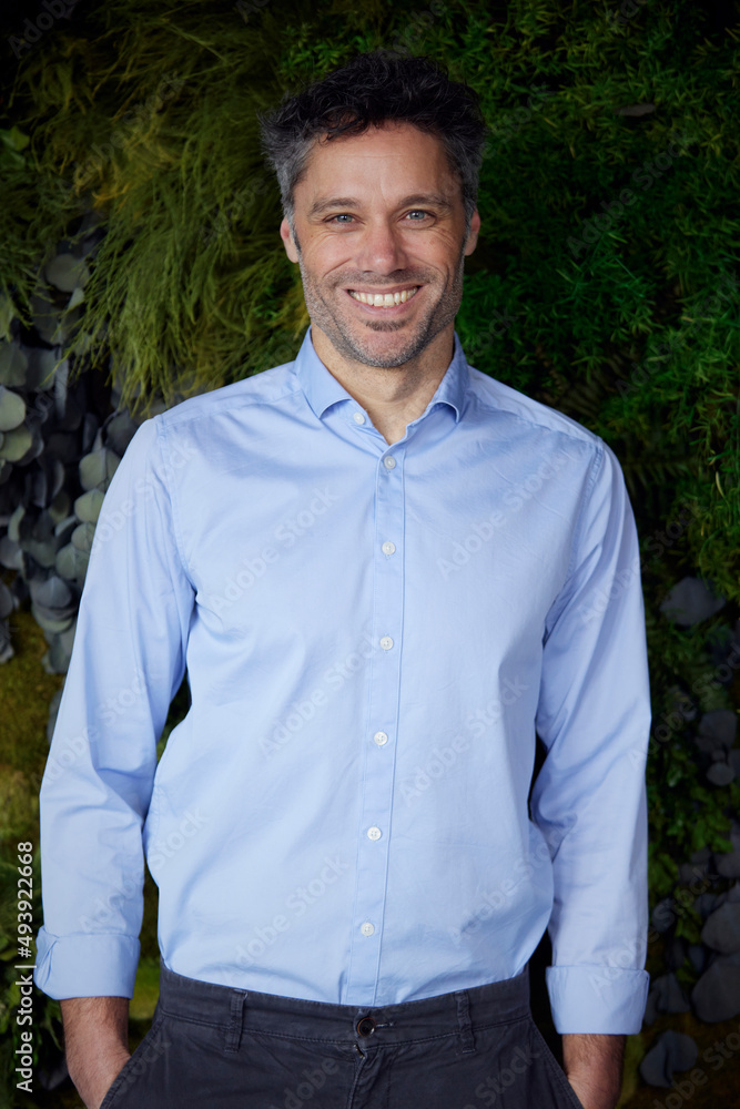 Happy businessman with hands in pockets in front of plants Happy businessman with hands in pockets in front of plants