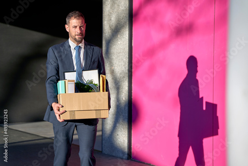 Businessman carrying box of personal belongings by wall on footpath