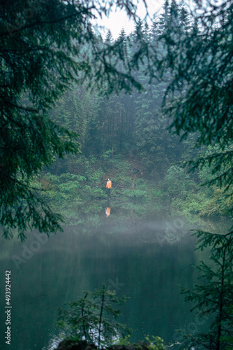 man hiker in yellow raincoat looking at mountain lake