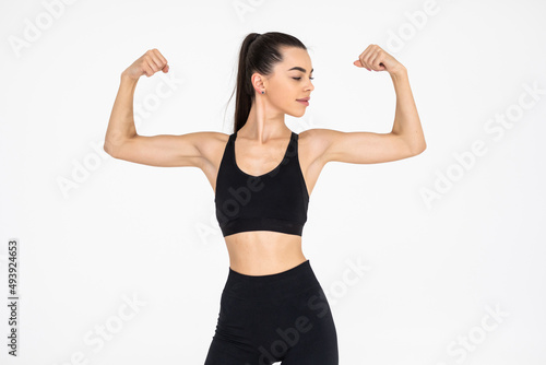 Cheerfully smiling mixed race sporty woman demonstrating biceps on white background