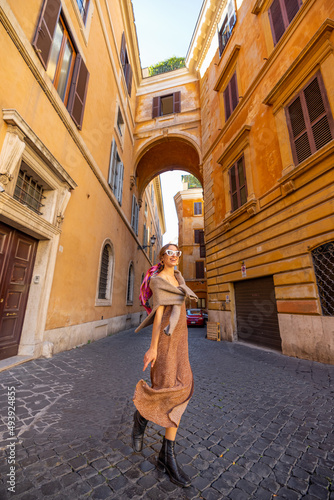 Woman walks on narrow old street with beautiful buildings and arch ahead in Rome. Portrait of a happy stylish woman in Rome. Wide angle view