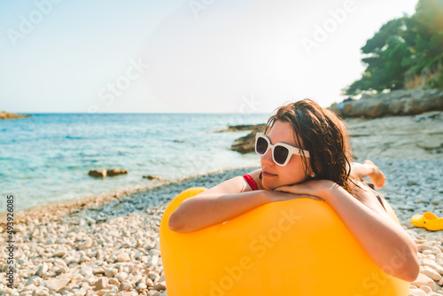 woman sunbathing at sea beach laying on yellow air sofa © phpetrunina14