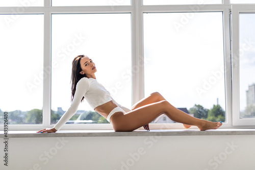 Beautiful daydreamer. Beautiful young woman in lingerie with smile while sitting at windowsill at home