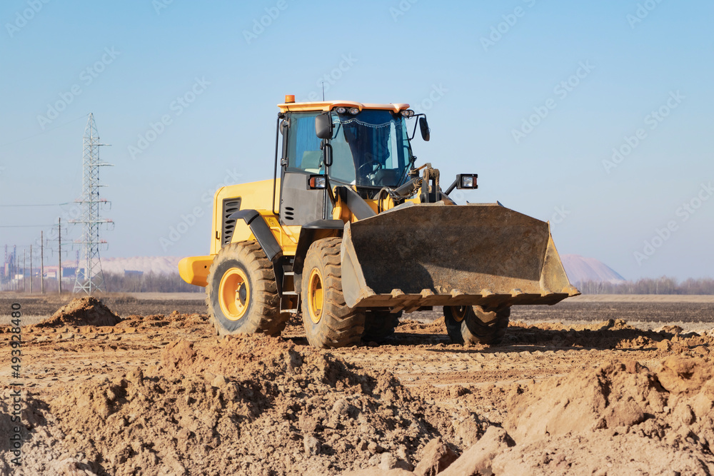 Bulldozer or loader moves the earth at the construction site against the blue sky. An earthmoving machine is leveling the site. Construction heavy equipment for earthworks. Bulldozer or loader moves the earth at the construction site against the blue sky. An earthmoving machine is leveling the site. Construction heavy equipment for earthworks.