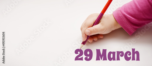 A child's hand writes 29 march in a lilac pencil. Banner with copy space