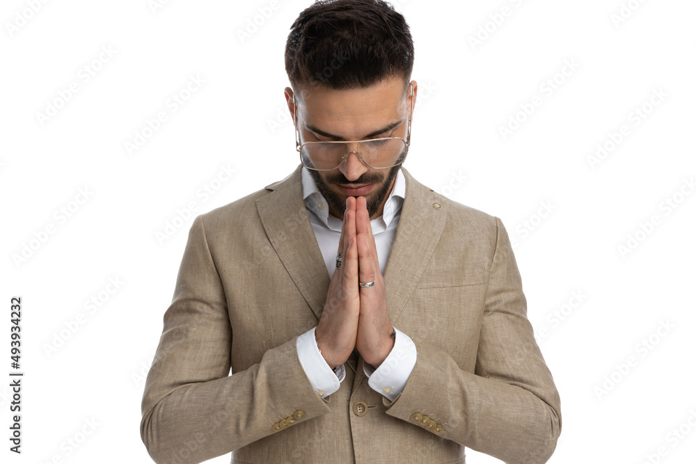 young businessman holding hands together, looking down young businessman holding hands together, looking down