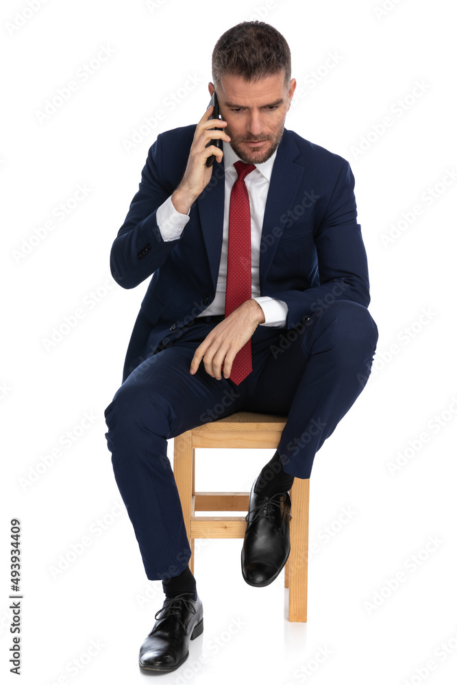 elegant unshaved businessman with elbow on knee talking on the phone elegant unshaved businessman with elbow on knee talking on the phone