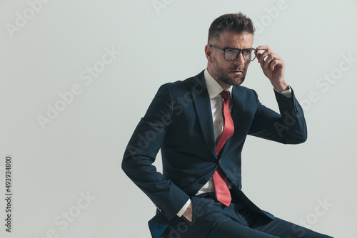 side view of seated man in his forties looking away and adjusting glasses © Viorel Sima