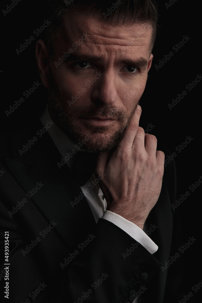 sexy bearded best man in tuxedo holding hand to chin and thinking sexy bearded best man in tuxedo holding hand to chin and thinking