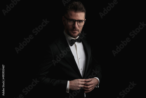 handsome bearded businessman with glasses buttoning tuxedo