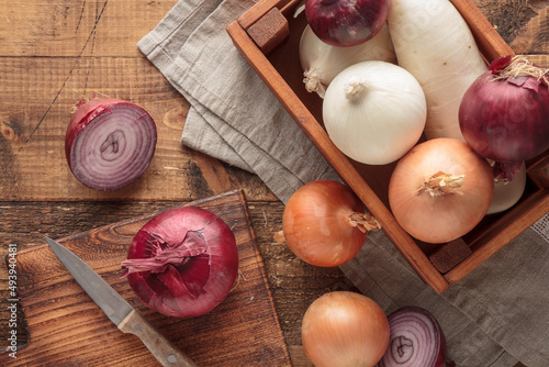 Different sorts of onion on a wooden background and a box, top view close up, rustic style, home kitchen, farming concept