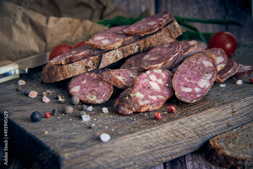 Smoked sausage, cut into pieces, sprinkled with spices, lies on a wooden cutting board.