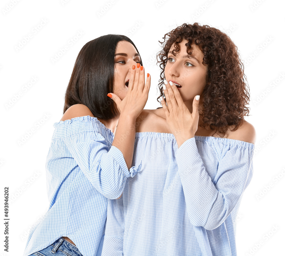 Young woman telling secret to her sister on white background Young woman telling secret to her sister on white background