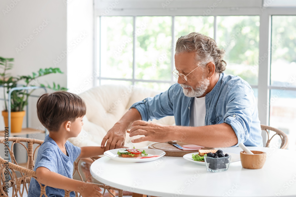 Little boy having breakfast with his grandfather at table in kitchen Little boy having breakfast with his grandfather at table in kitchen