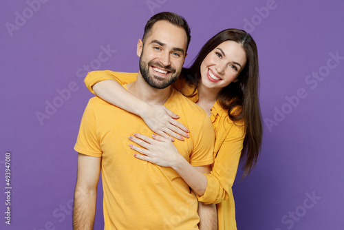Young smiling happy cheerful nice lovely couple two friends family man woman 20s together wearing yellow casual clothes looking camera hud cuddle isolated on plain violet background studio portrait