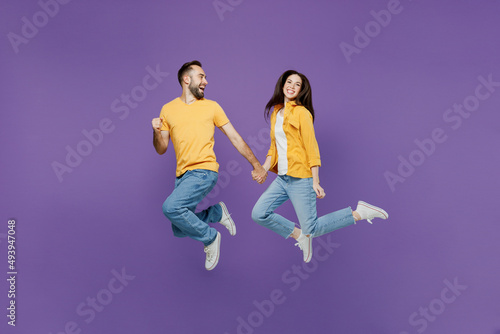 Full length young excited cheerful fun overjoyed couple two friends family man woman together in yellow casual clothes jump high run fast hurry up isolated on plain violet background studio portrait