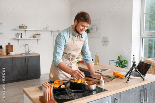 Young man cooking vegetables while following video tutorial in kitchen
