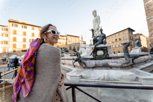 Young woman traveling famous italian landmarks in Florence city. Enjoying beautiful architecture and Neptuine fountain on Signoria square. Woman dressed in Italian style with colorful scarf in hair photo