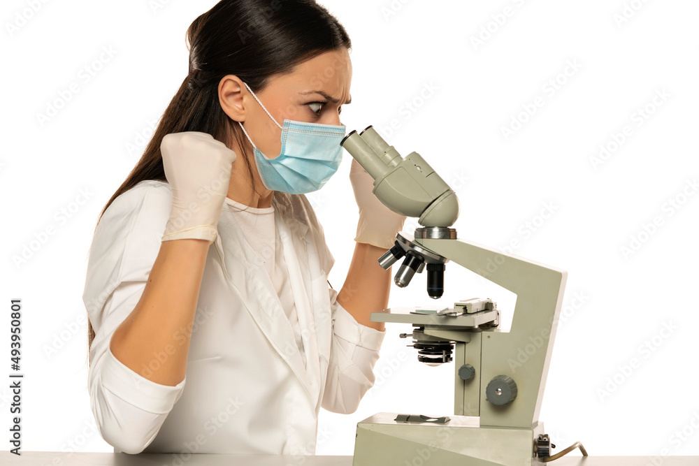 Angry nervous female scientist with protective face mask looking through a microscope, Angry nervous female scientist with protective face mask looking through a microscope,