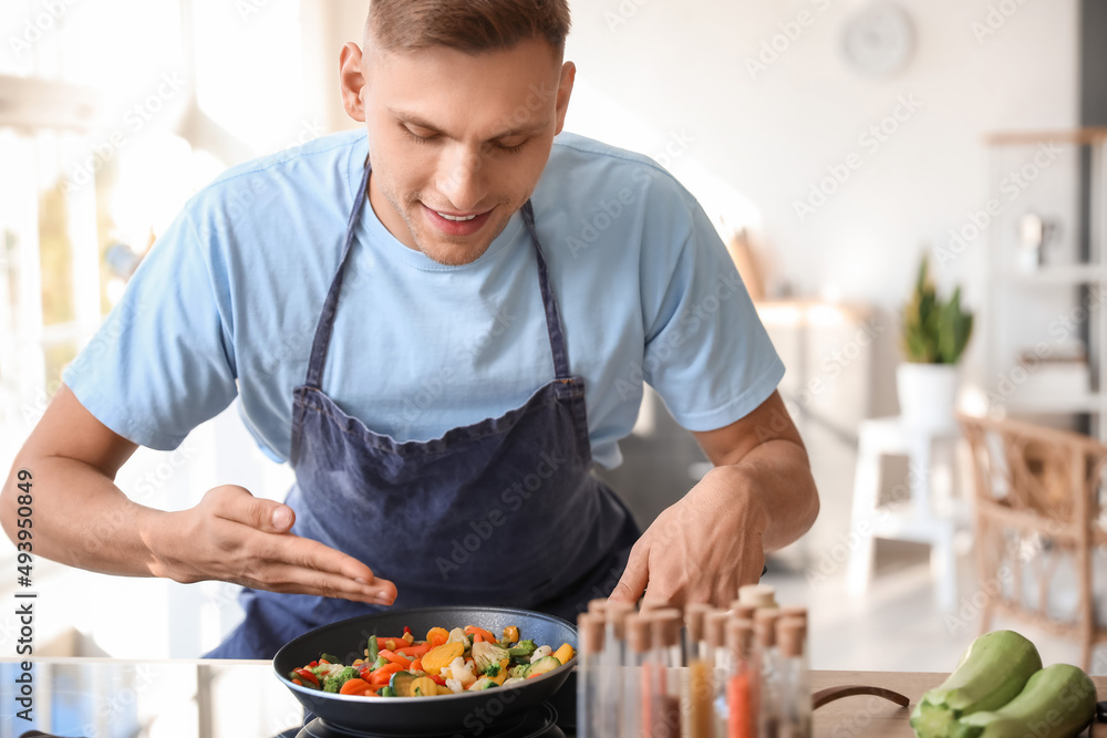 Young man frying tasty vegetables in kitchen