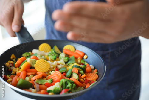 Young man holding frying pan with tasty vegetables in kitchen, closeup