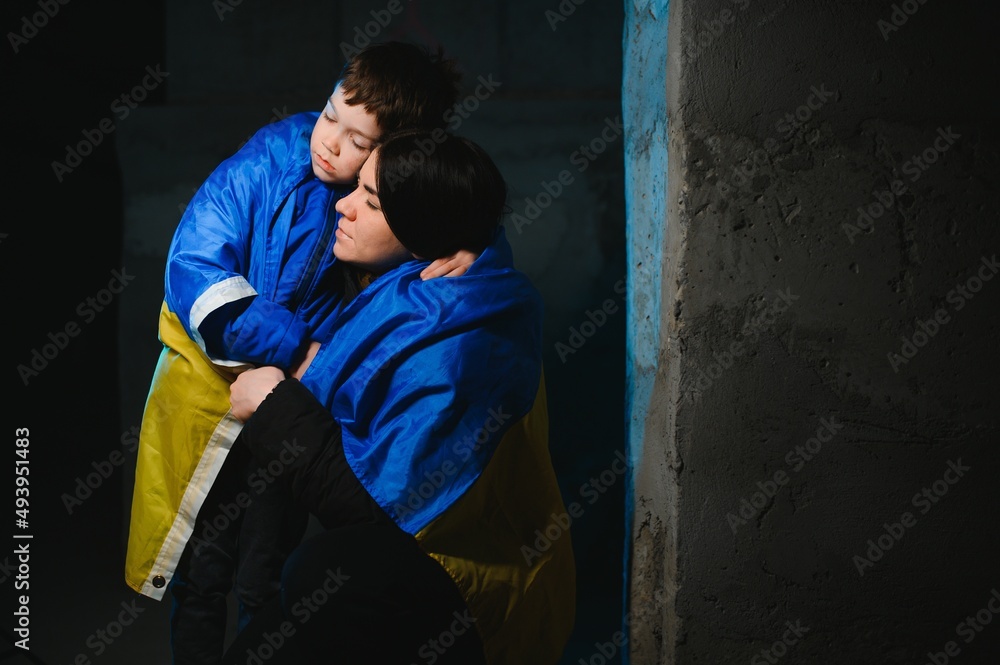 Sad mother hugging her son, both wearing Ukrainian national colors on black background.