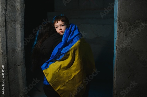 Sad mother hugging her son, both wearing Ukrainian national colors on black background. © Serhii