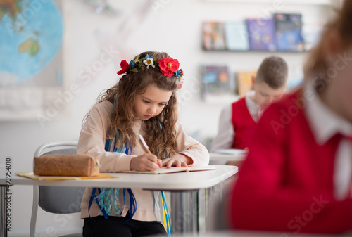 Little sad Ukrainian girl writing in classroom during class, concept of enrolling Ukrainian kids to schools. photo