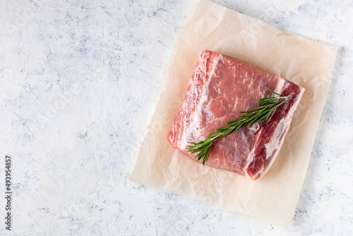 A piece of raw fresh pork with rosemary on a vax paper on white background. Meat with spices photo