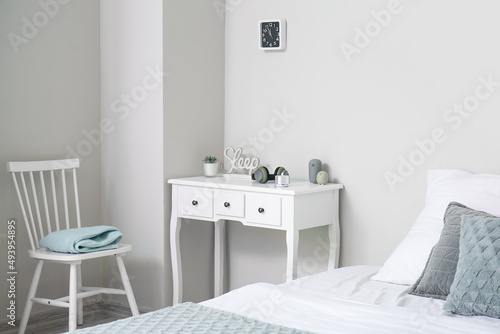Table with wireless portable speaker and headphones near light wall in bedroom