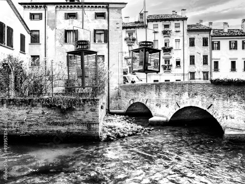 Vista de um restaurante em Treviso, Itália. Um rio em frente a um restaurante.  Ponte milenar de tijolos. Arandelas com velas roxas. Construções milenares. Arquitetura italiana. photo