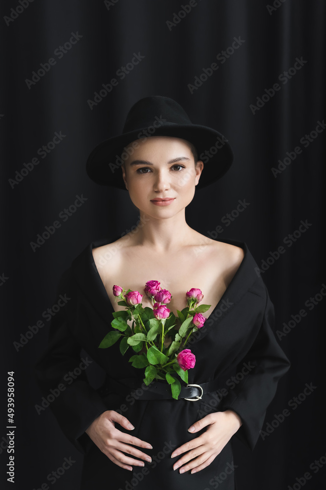 Fototapeta premium front view of young woman with pink roses in black blazer on dark background.