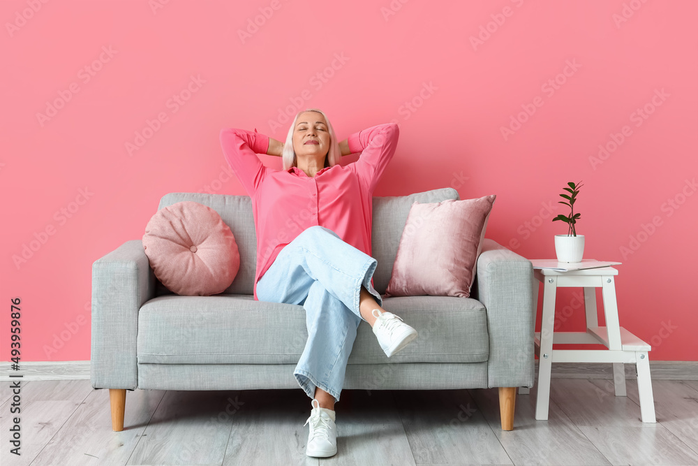 Mature woman relaxing on sofa near pink wall Mature woman relaxing on sofa near pink wall