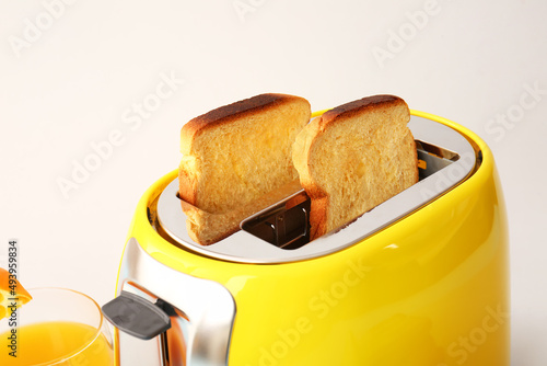 Modern toaster with bread slices and glass of juice on light background, closeup