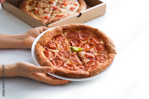Selective focus of the circle of pepperoni pizza on a plate in the boy's hands. The concept of a snack for children, take off, take away.