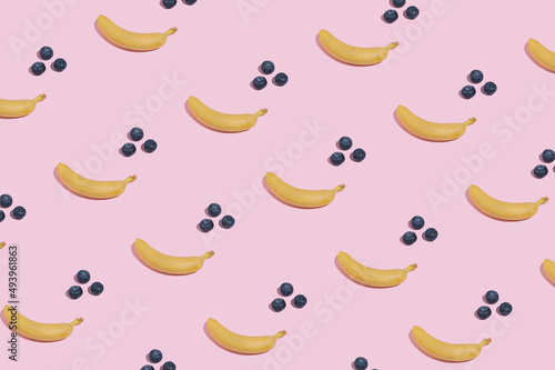Modern minimal pattern with yellow bananas and blueberries on bright pink background. Trendy summer fruit aesthetic.