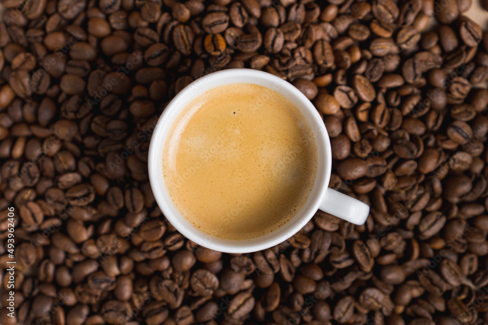 Small white coffee cup with espresso crema on roasted beans background. Selective focus Small white coffee cup with espresso crema on roasted beans background. Selective focus