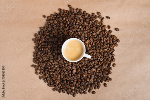 Small white coffee cup with espresso crema on roasted beans at brown background. Mock up