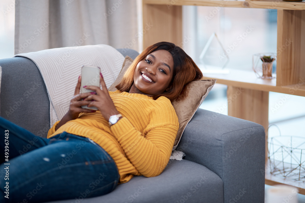 Obraz premium Home is my happy place. Shot of an attractive young woman using her cellphone while relaxing on the sofa at home.