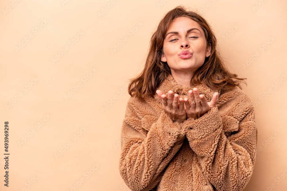 Young caucasian woman isolated on beige background folding lips and holding palms to send air kiss. Young caucasian woman isolated on beige background folding lips and holding palms to send air kiss.