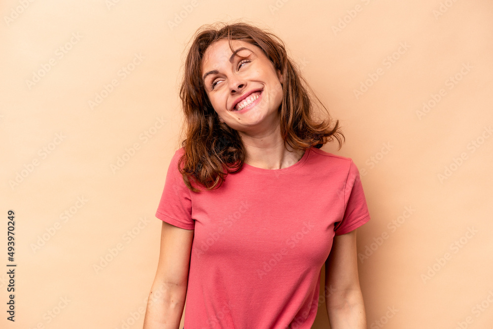 Young caucasian woman isolated on beige background laughs and closes eyes, feels relaxed and happy. Young caucasian woman isolated on beige background laughs and closes eyes, feels relaxed and happy.