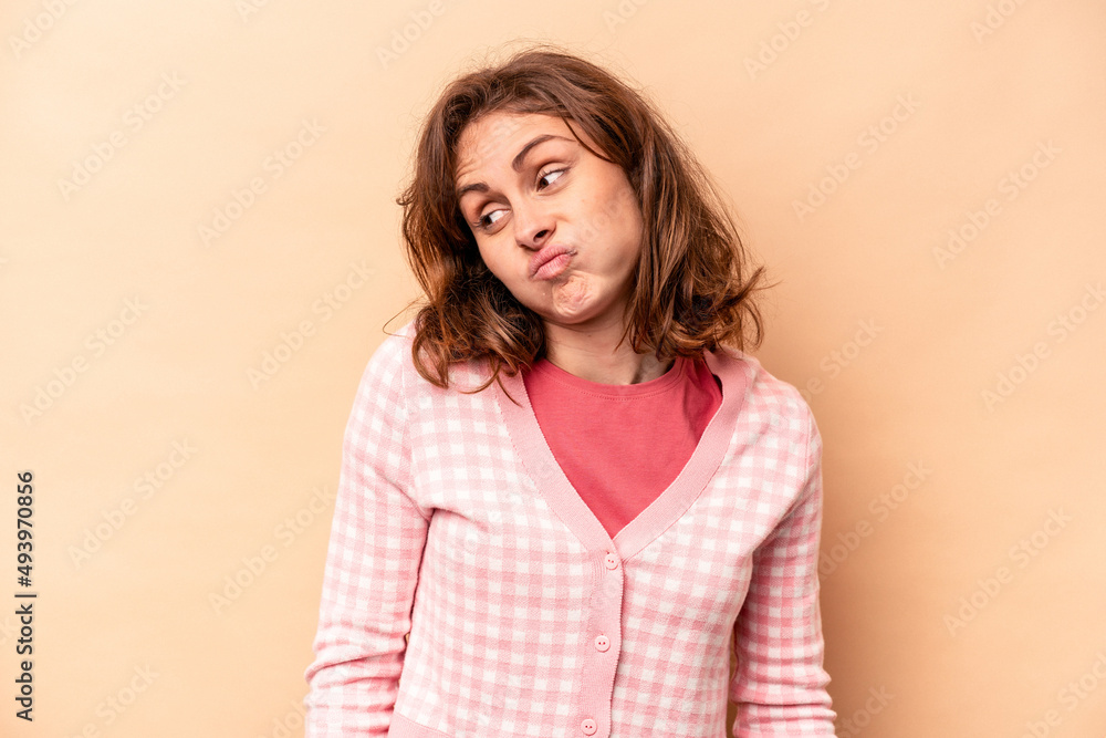 Young caucasian woman isolated on beige background shrugs shoulders and open eyes confused. Young caucasian woman isolated on beige background shrugs shoulders and open eyes confused.
