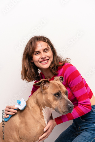 Young caucasian woman combing her dog isolated on white background